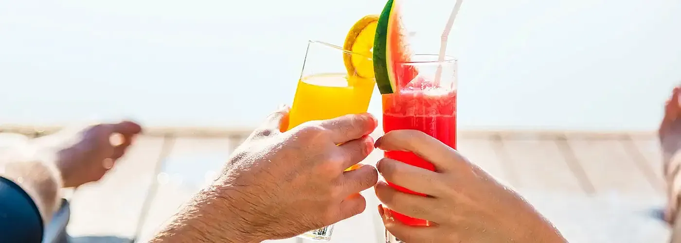 two sunbathing people clinking glasses full of cocktails